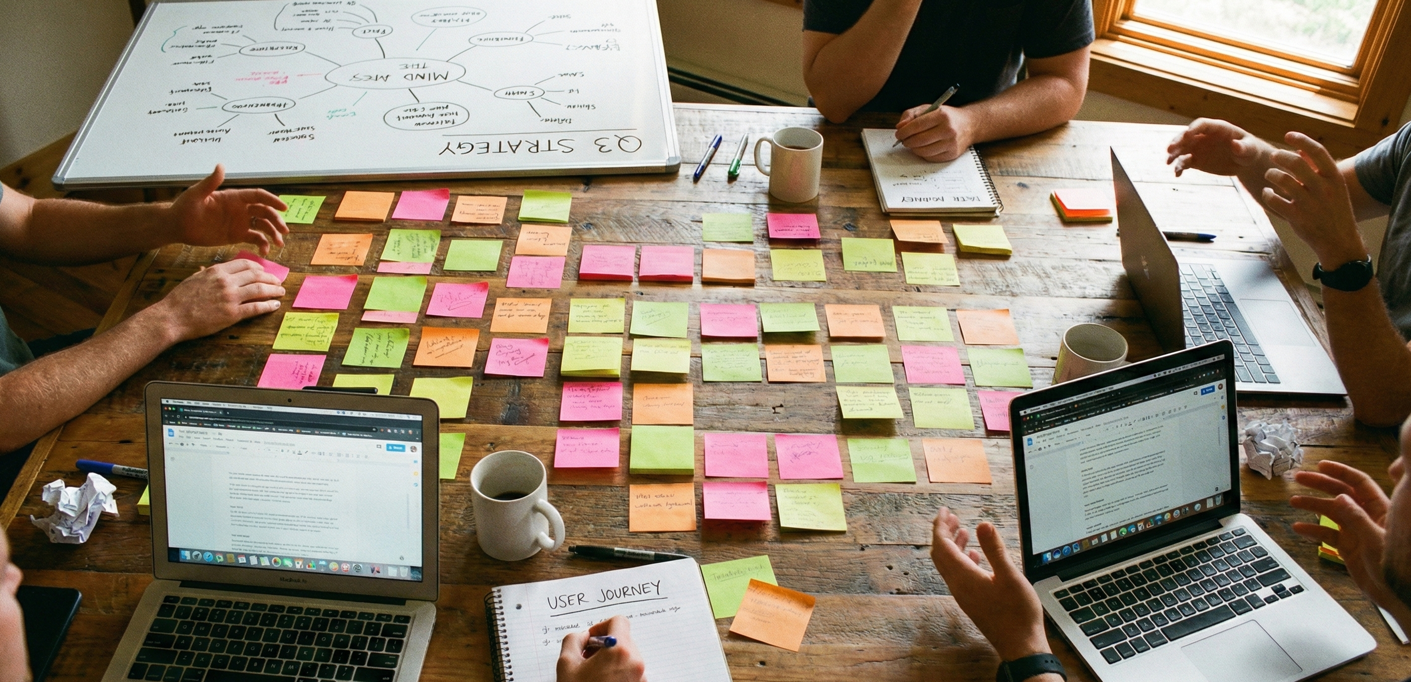 Brainstorming session at a wooden table with sticky notes and laptops